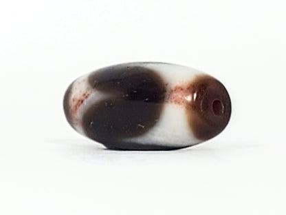 End cap of antique Tasso dzi At-093024-TaBS3, deep brown agate tip with centred drill hole, wide barrel body, cream Tasso zones with bloodspot inclusions visible, unretouched
