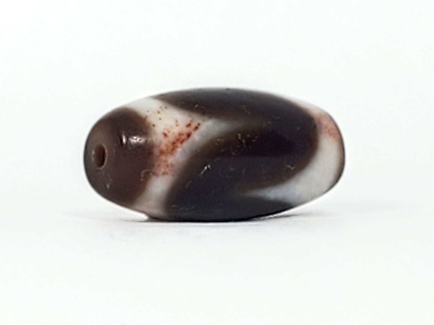 Angled view of antique Tasso dzi At-093024-TaBS3, deep brown agate body, broad cream Tasso wave, bloodspot inclusions, natural weathering marks, 29.4mm × 14.0mm, unretouched