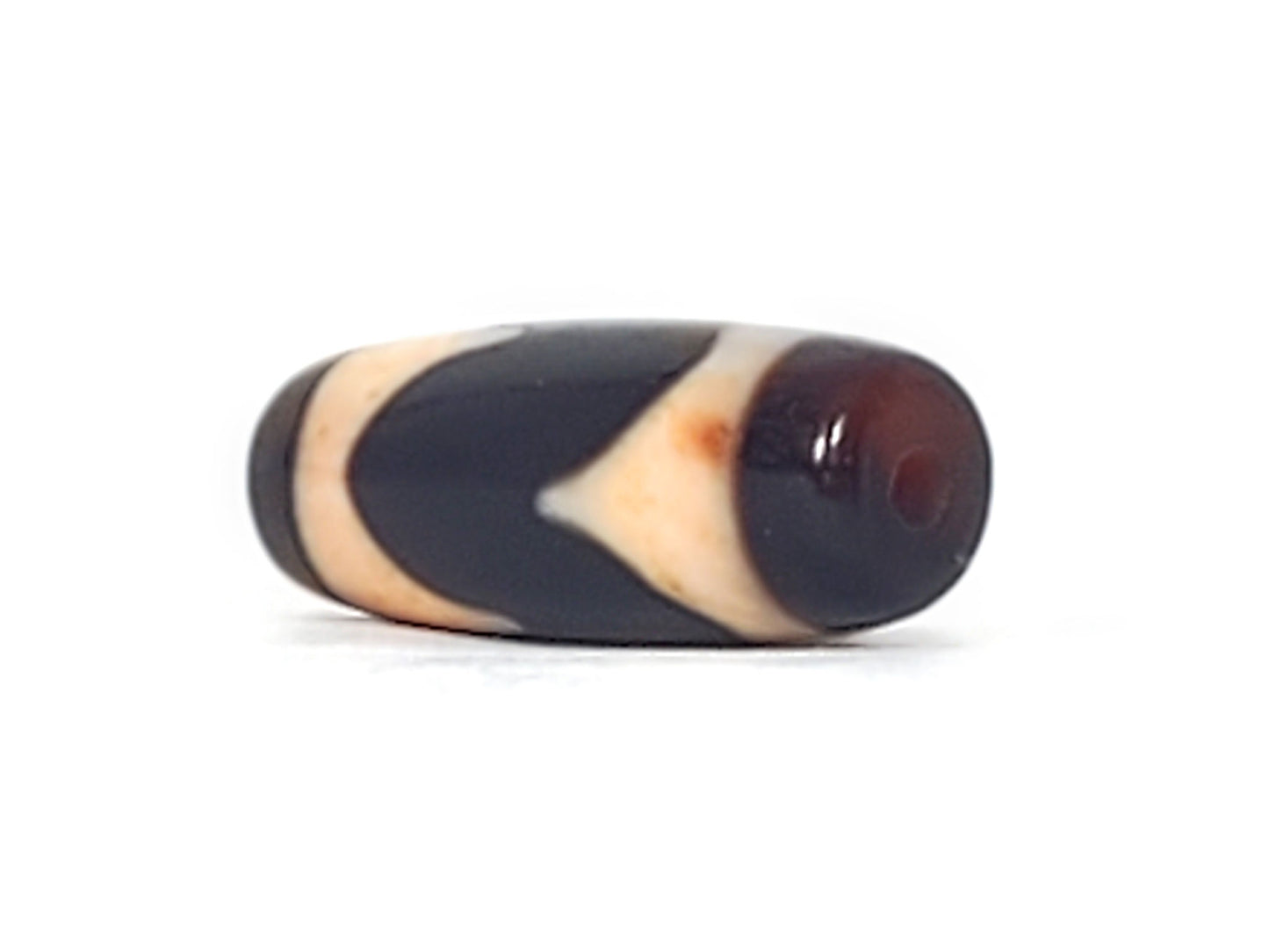 Opposite end cap of antique Tasso dzi At-092924-TaBS2, pitch-black agate tip, drill hole centred, cream Tasso zones with bloodspot inclusions visible, 28.7mm × 11.2mm