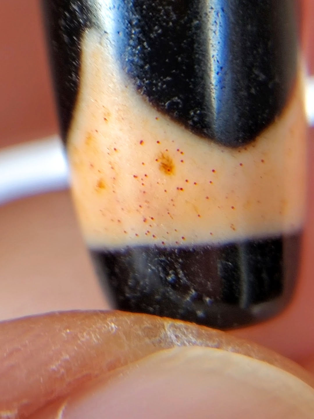 Extreme macro of antique Tasso dzi At-092924-TaBS2 showing cinnabar bloodspot constellation — vermilion-red micro-dots and rust-orange formations in cream agate field, unretouched