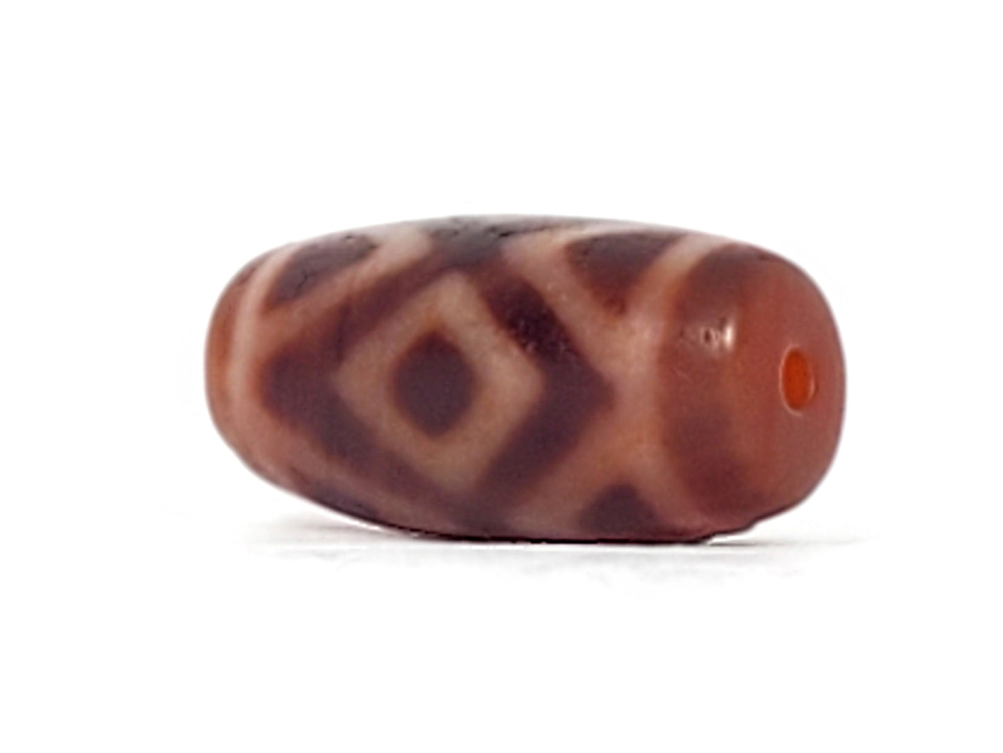 Three-quarter view of antique Three Diamond Eye Tiger Tooth dzi At-053126-3DETT, vivid terracotta-red end cap with orange drill hole, diamond motif on body, 27.5mm × 13.0mm, unretouched