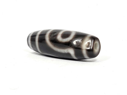 Three-quarter view of antique two eye dzi At-033126-2E4, pitch-black end cap with cream-ringed drill hole, torpedo body, 37.3mm × 12.8mm, unretouched photography