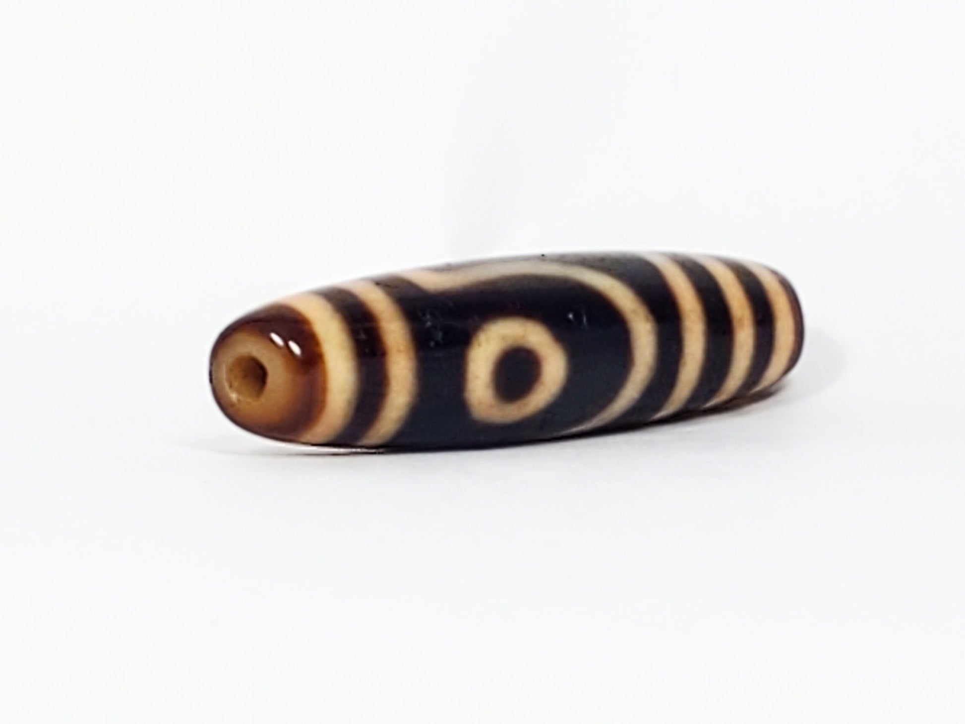 Opposite end of antique Tibetan Two Eye dzi bead showing drill hole in warm brown cap and eye motif, At-082624-2E