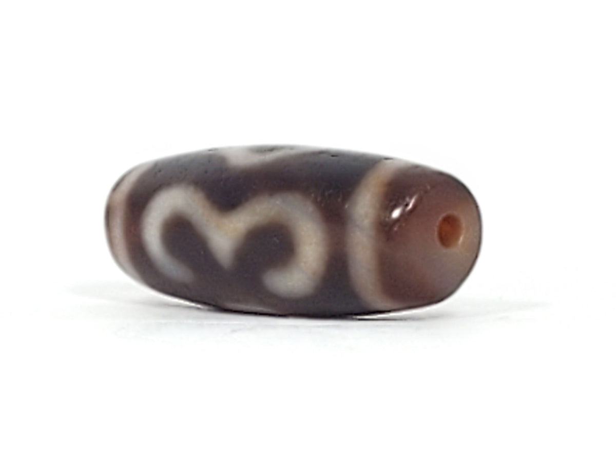 End cap of antique Double Bat Two Eye dzi At-053026-DB2E, dark brown agate tip with centred drill hole, compact barrel body, cream motif visible, bloodspots, unretouched photography