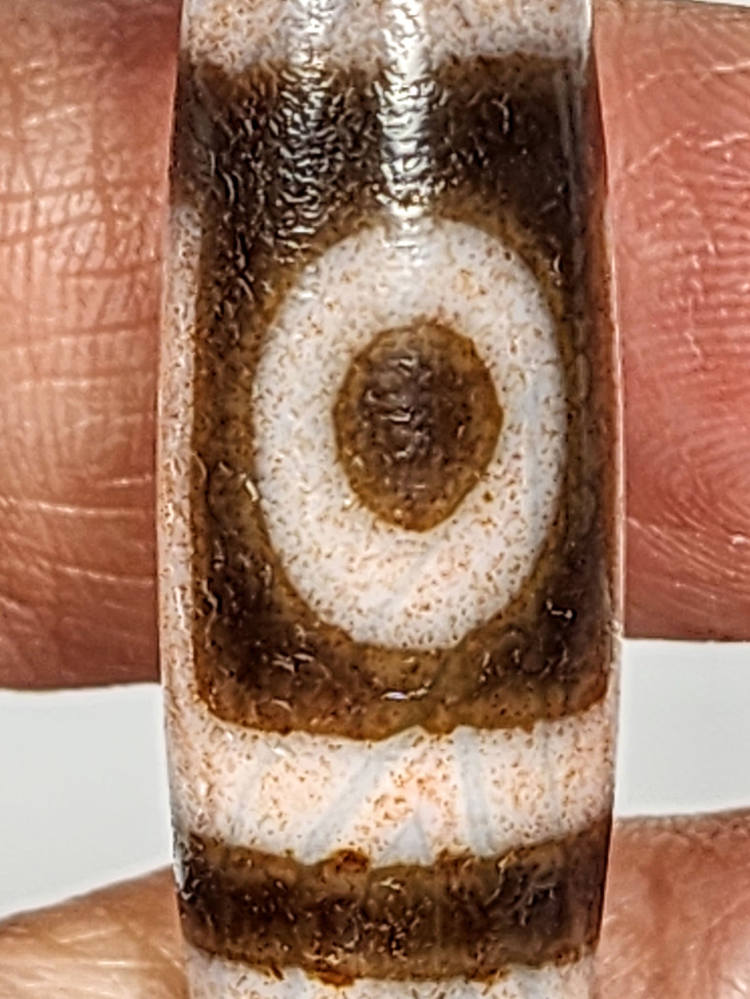 Macro of antique two eye dzi At-092724-2EBS showing second eye and stripe zones, pervasive rust-orange cinnabar saturation in dark agate, cinnabar dusting on cream bands, unretouched