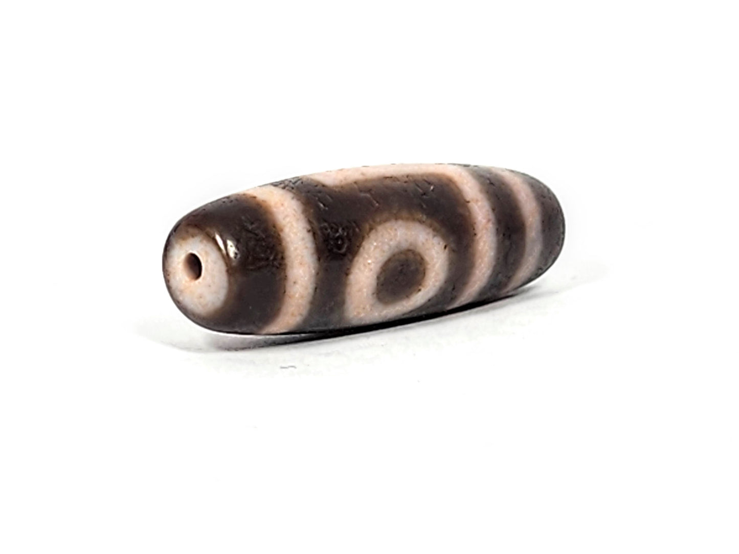 Three-quarter view of antique two eye dzi At-092724-2EBS, dark brown end cap with drill hole, one eye visible, warm dark brown torpedo body, 41.0mm × 13.0mm, unretouched