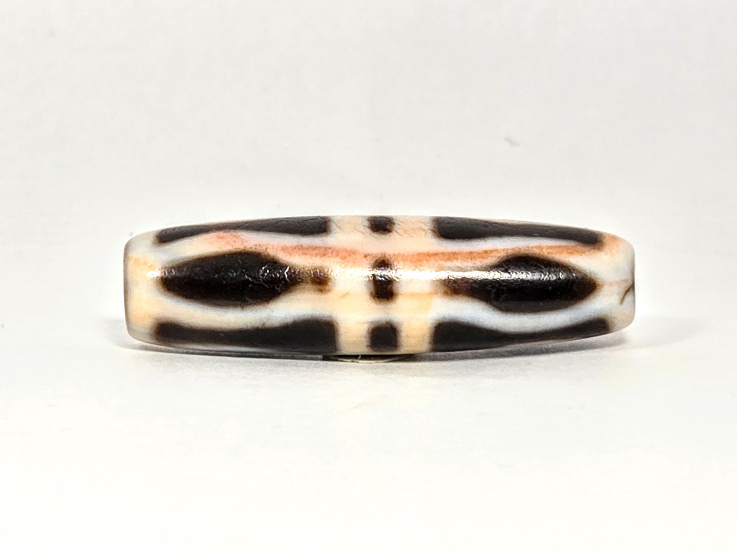 At-070626-3VjBS hero flat, triple vajra dzi, 42.8×12.1mm, cream-dominant ground, dark brown motif arms, unretouched