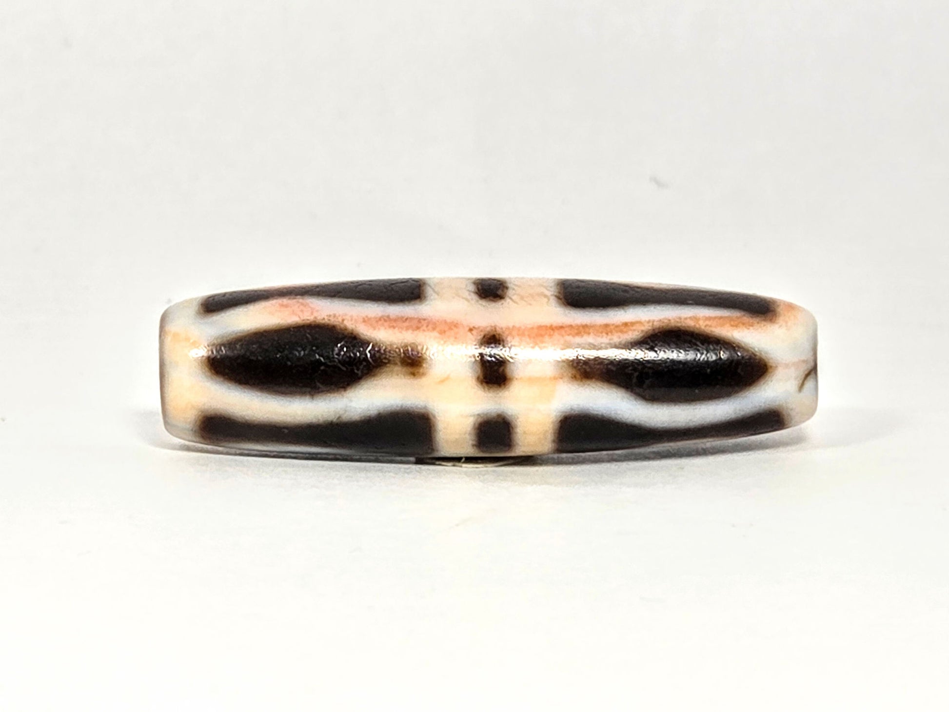 At-070626-3VjBS hero flat, triple vajra dzi, 42.8×12.1mm, cream-dominant ground, dark brown motif arms, unretouched