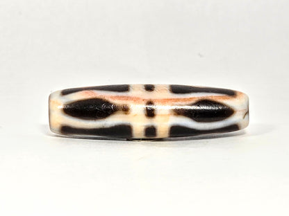 At-070626-3VjBS hero flat, triple vajra dzi, 42.8×12.1mm, cream-dominant ground, dark brown motif arms, unretouched