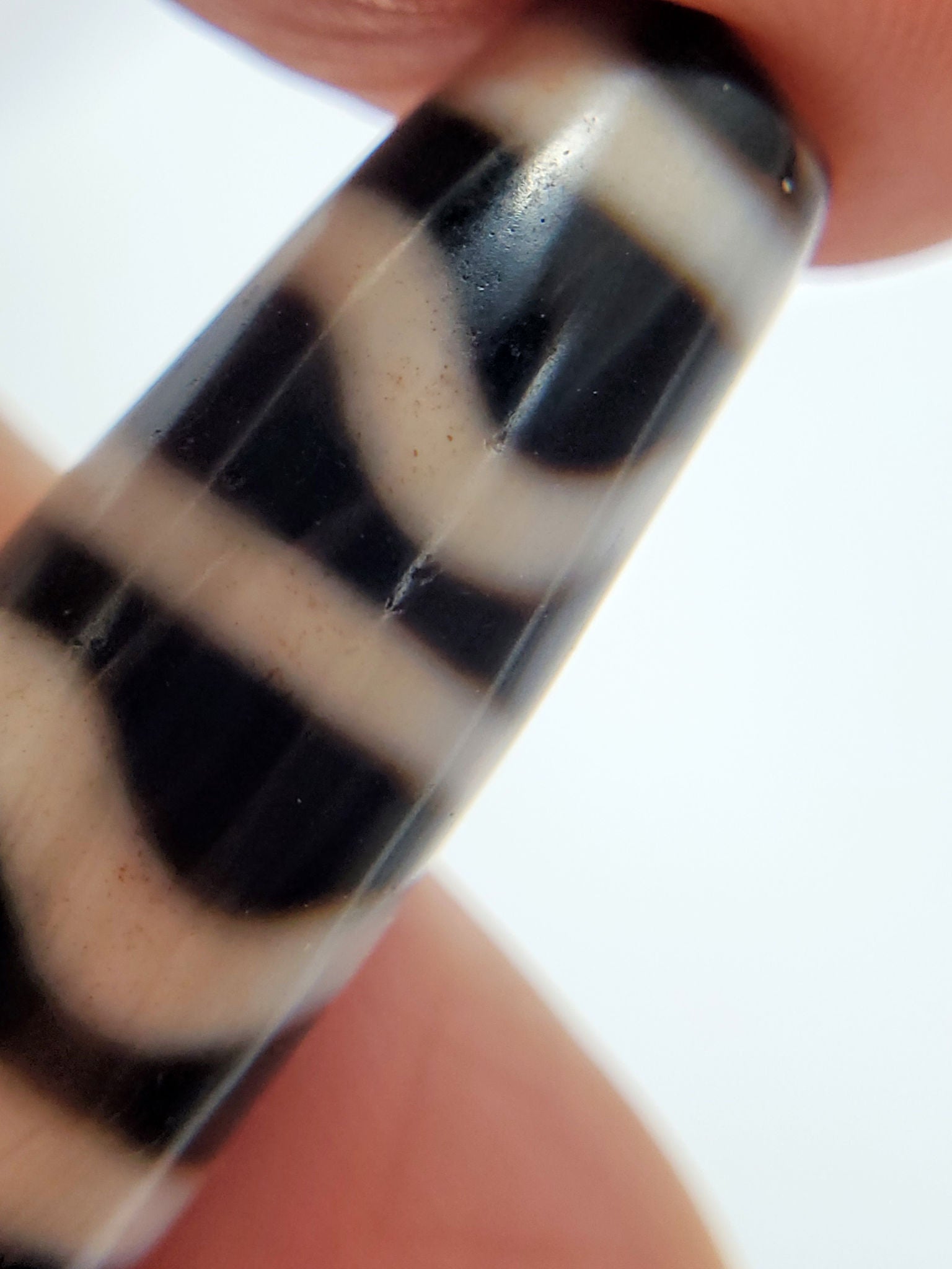 Hand-held macro of antique Wave Stripe dzi bead showing undulating white wave lines on black agate, At-052526-WS