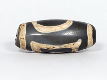At-022624-HEG, Face B showing paired wave-arc connector forms, warm cream on deep charcoal-grey agate, unretouched