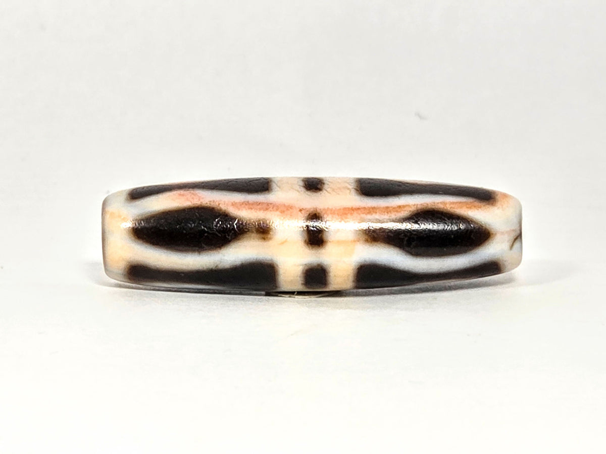At-070626-3VjBS hero flat, triple vajra dzi, 42.8×12.1mm, cream-dominant ground, dark brown motif arms, unretouched