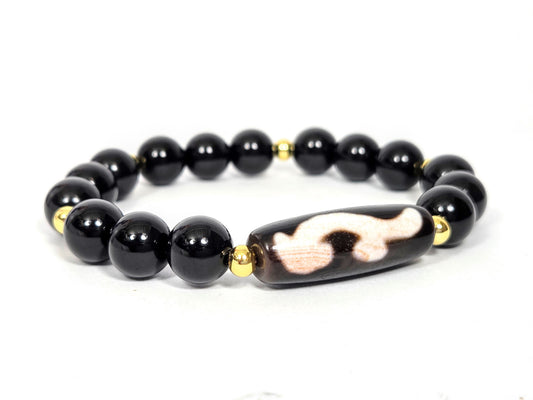Full bracelet view: vintage Ruyi dzi focal bead centred on a strand of polished black agate rounds with gold-plated accent beads, photographed on white — Ancient Dzi Shop