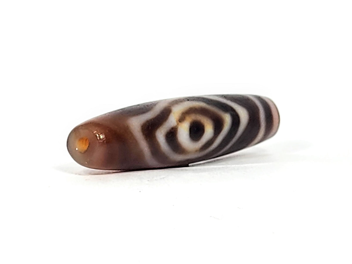 Antique eye-in-eye heaven gate dzi — opposite end, orange-amber drill cap visible at near tip, eye motif on body, At-0426-EIE