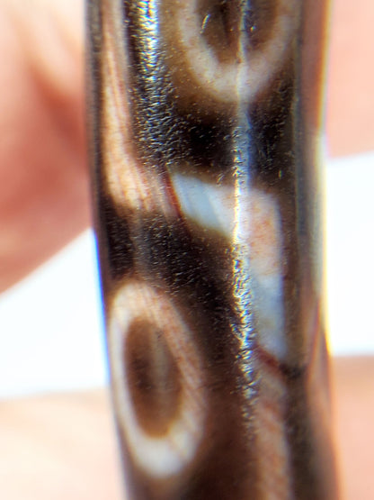 At-062926-9EBS angled view opposite end, 77.0mm nine eye dzi, drill hole visible, deep dark brown agate, unretouched