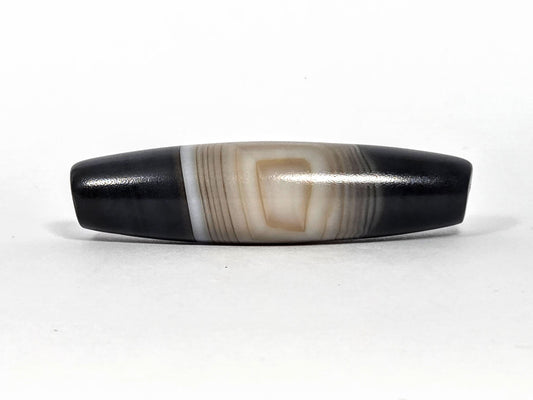 N-N-080426-1E5 natural one eye dzi bead 54.4×14.1mm, Face A showing resolved concentric oval eye in warm beige banding against pitch-black ends, unretouched