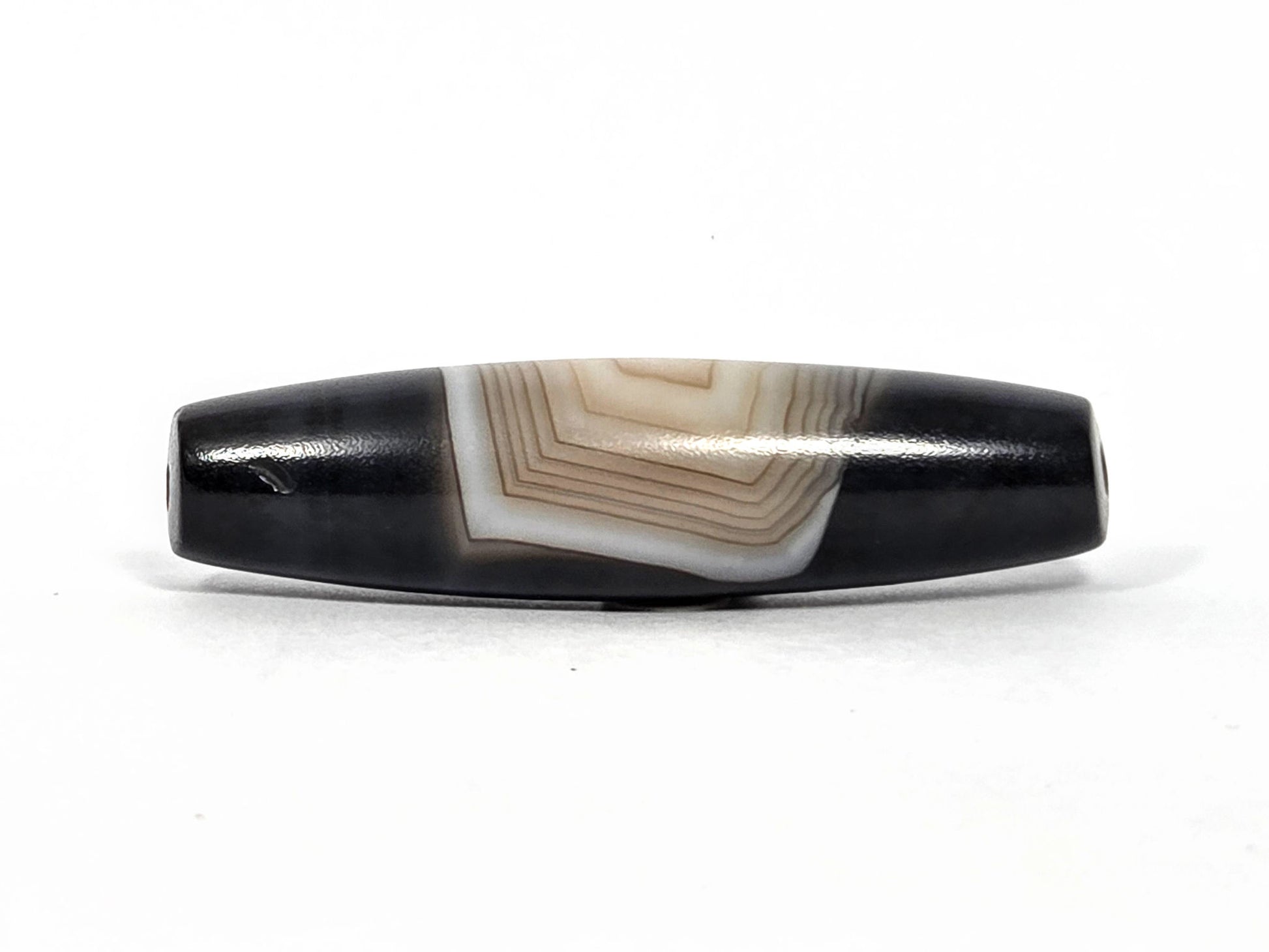N-N-080426-1E5 natural one eye dzi bead 54.4×14.1mm, Face B showing parallel banding lines and stepped concentric pattern from this angle, unretouched