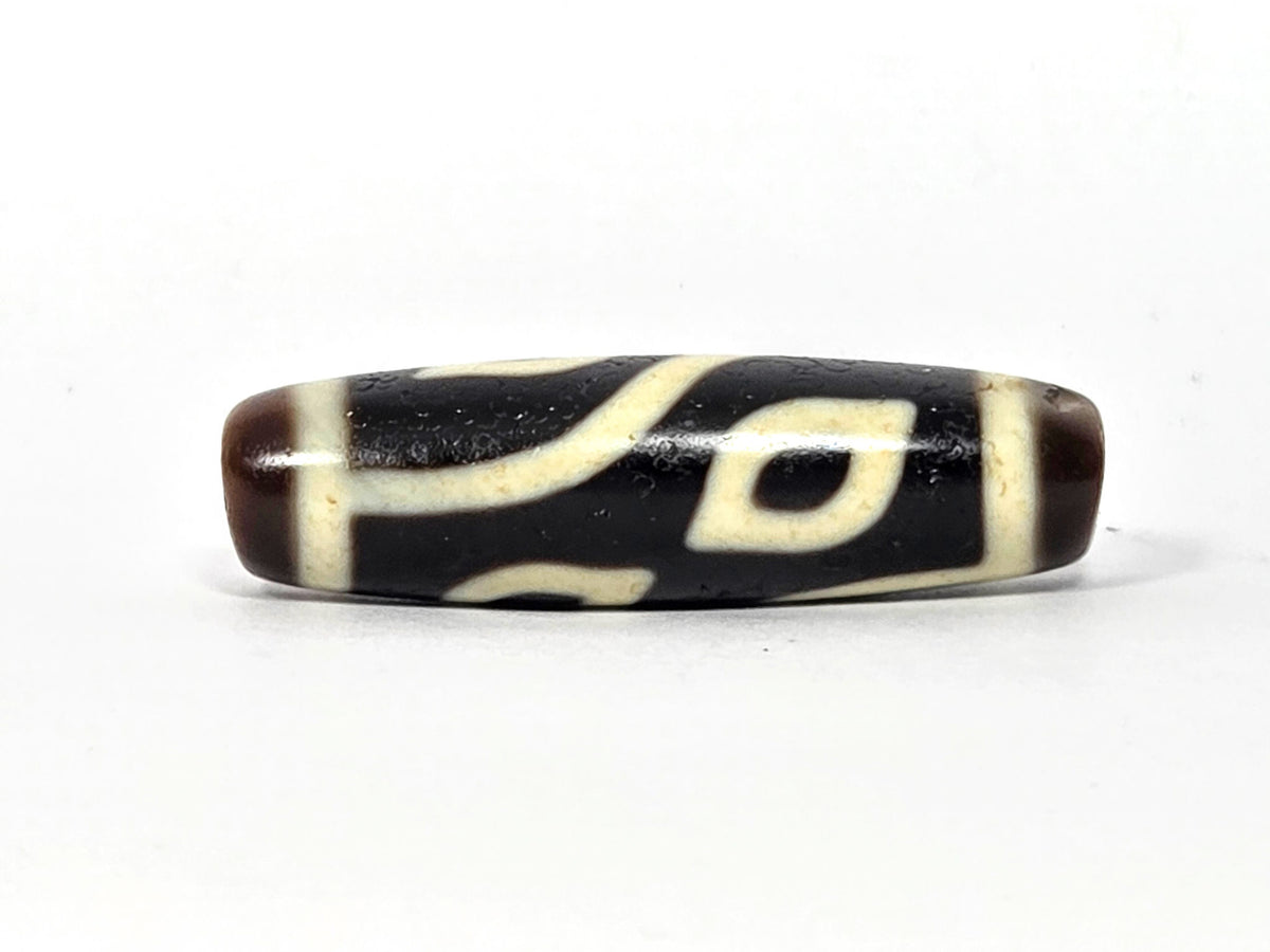 Four-eye dzi bead, dark brown and black agate, cream white eye motifs, elongated barrel shape, aged patina, 40mm