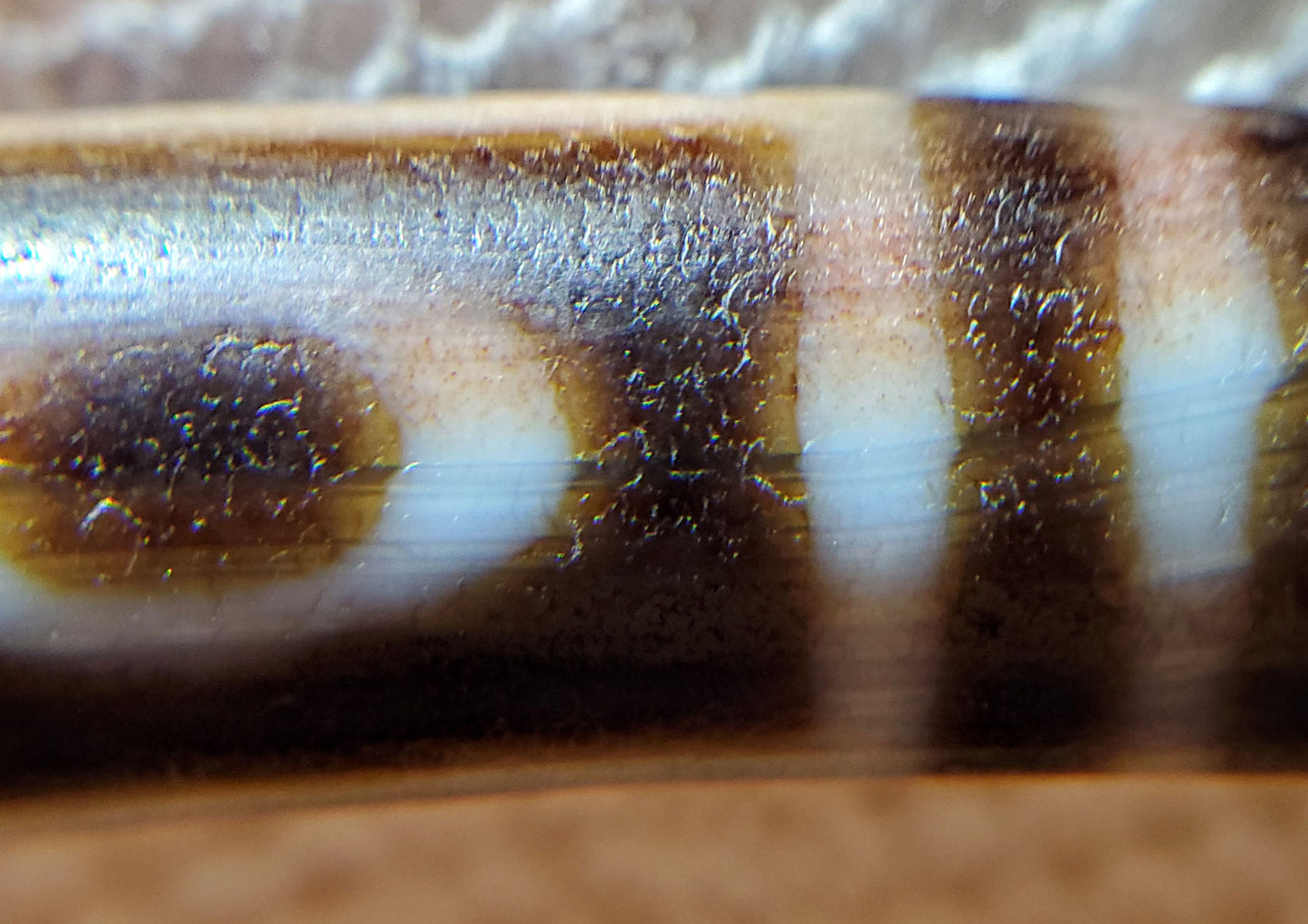 Macro: ancient dzi eye zone — micro-crystalline surface weathering and brown bloodspot pooling, Anc-0426-1EMt