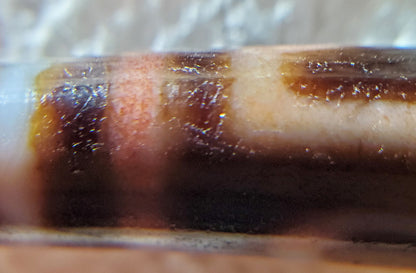 Macro: ancient dzi stripe field — red-brown iron oxide bloodspot bleeding into white zone, Anc-0426-1EMt