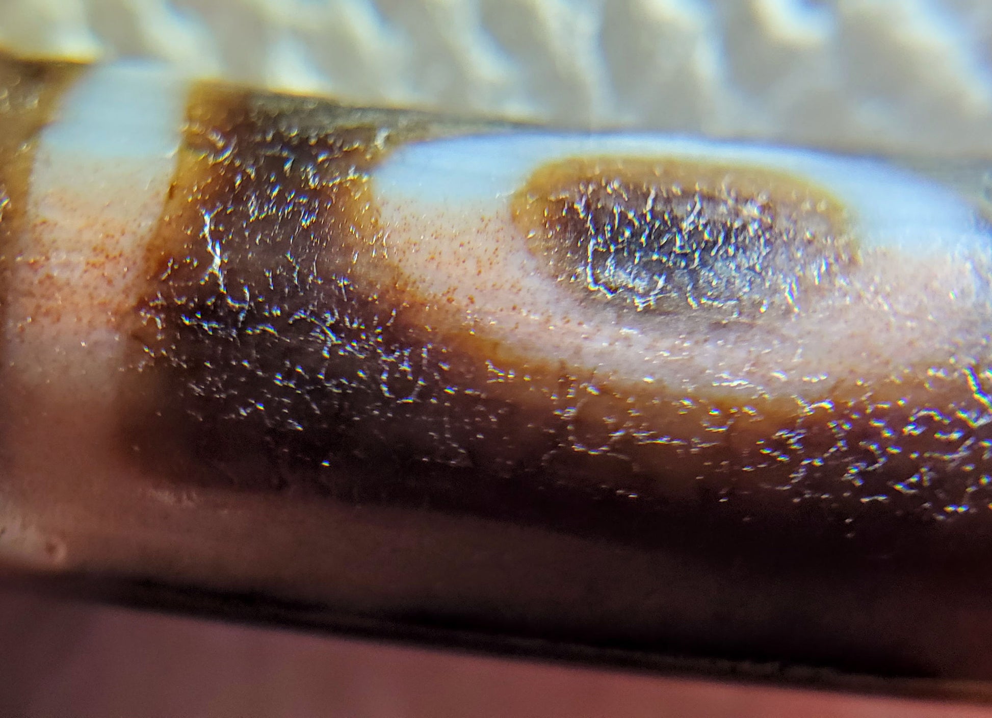Macro: ancient dzi eye ring — brown bloodspot pooling inside oval eye, deep crystalline age pitting, Anc-0426-1EMt