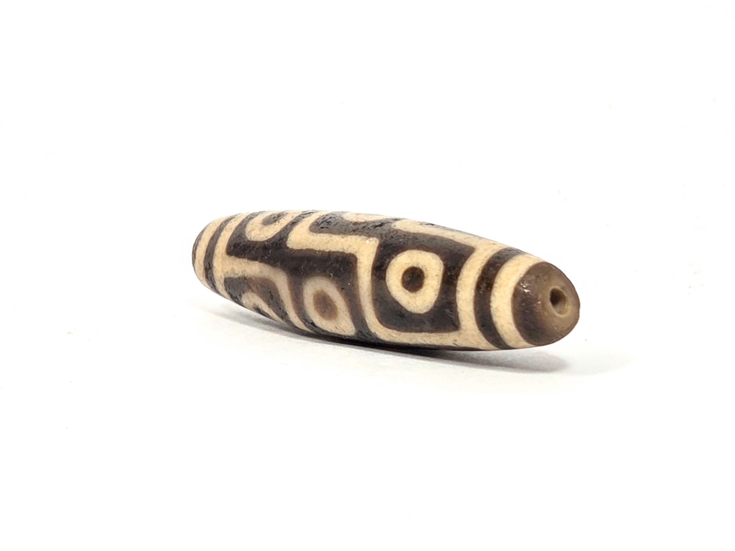 Ac-032326-9E5 right drill hole end, warm sandy-tan end cap and interior, nine-eye motif wrapping body, unretouched