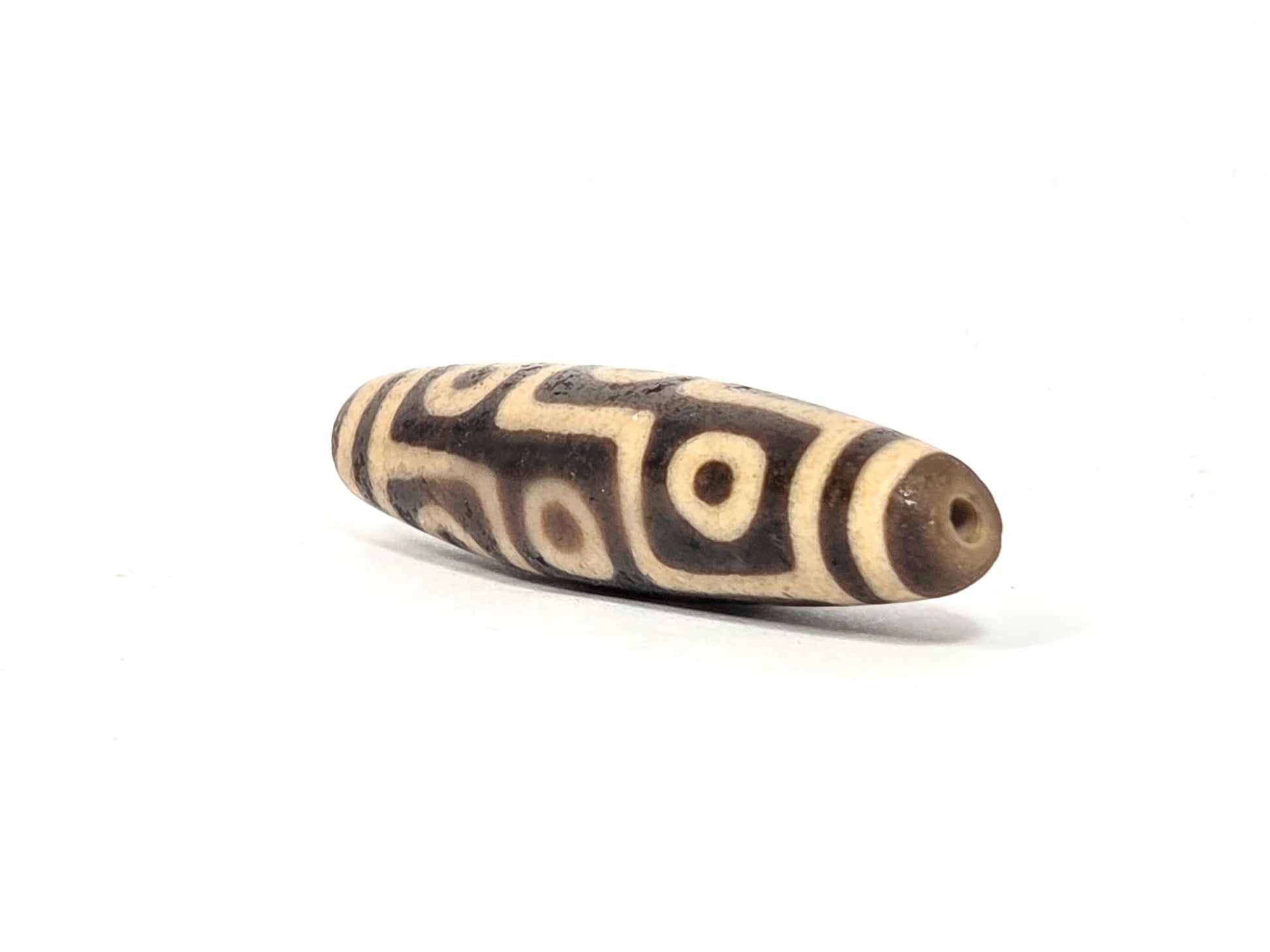 Ac-032326-9E5 right drill hole end, warm sandy-tan end cap and interior, nine-eye motif wrapping body, unretouched