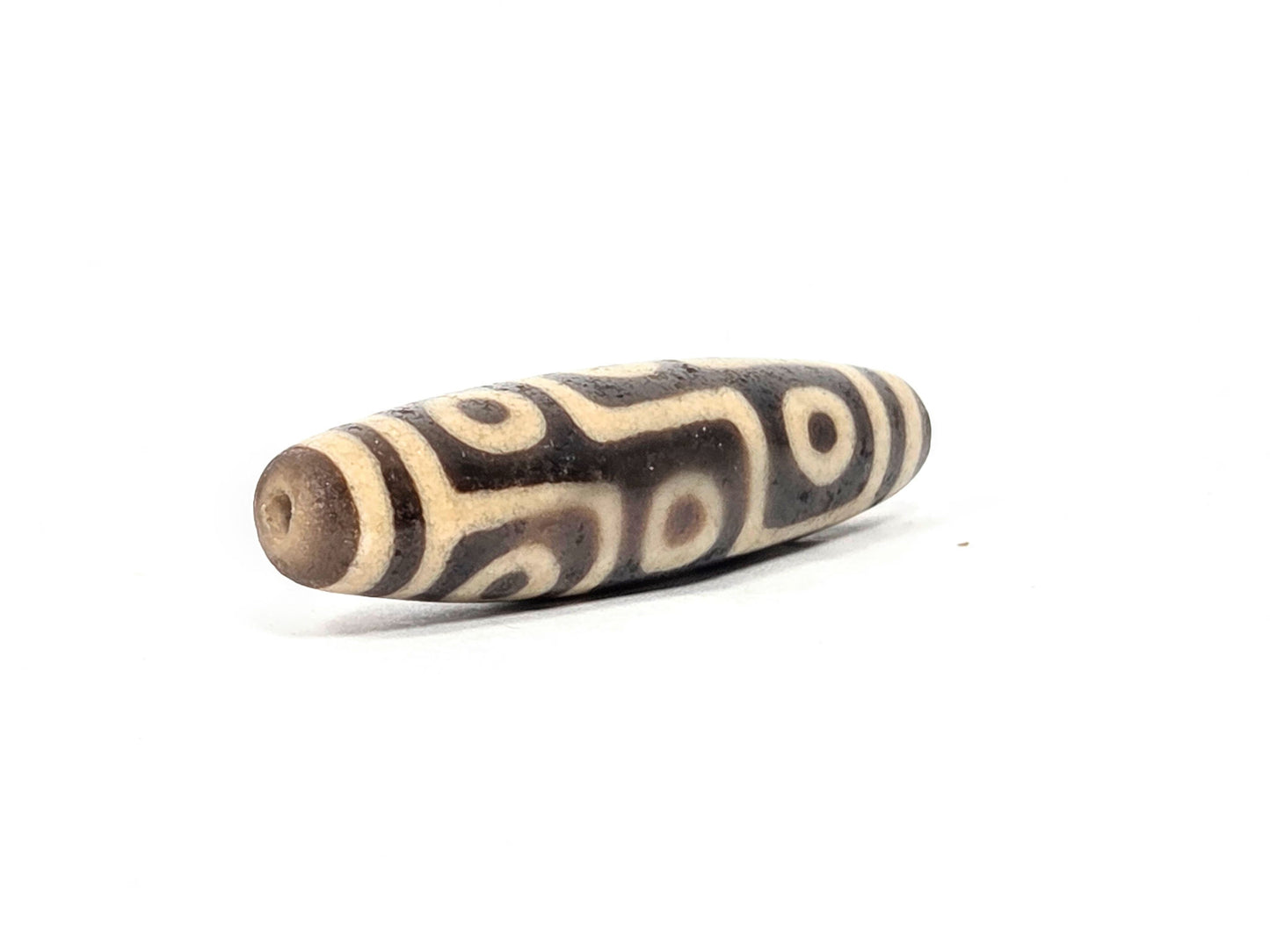 Ac-032326-9E5 left drill hole end, sandy-tan tip, age-granular cream-white surface texture visible, unretouched