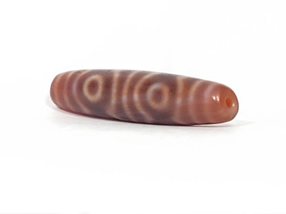 At-082624-6EBS, angled end-cap view, warm terracotta-rose cap, vivid orange-red drilled hole, six eye motif, unretouched