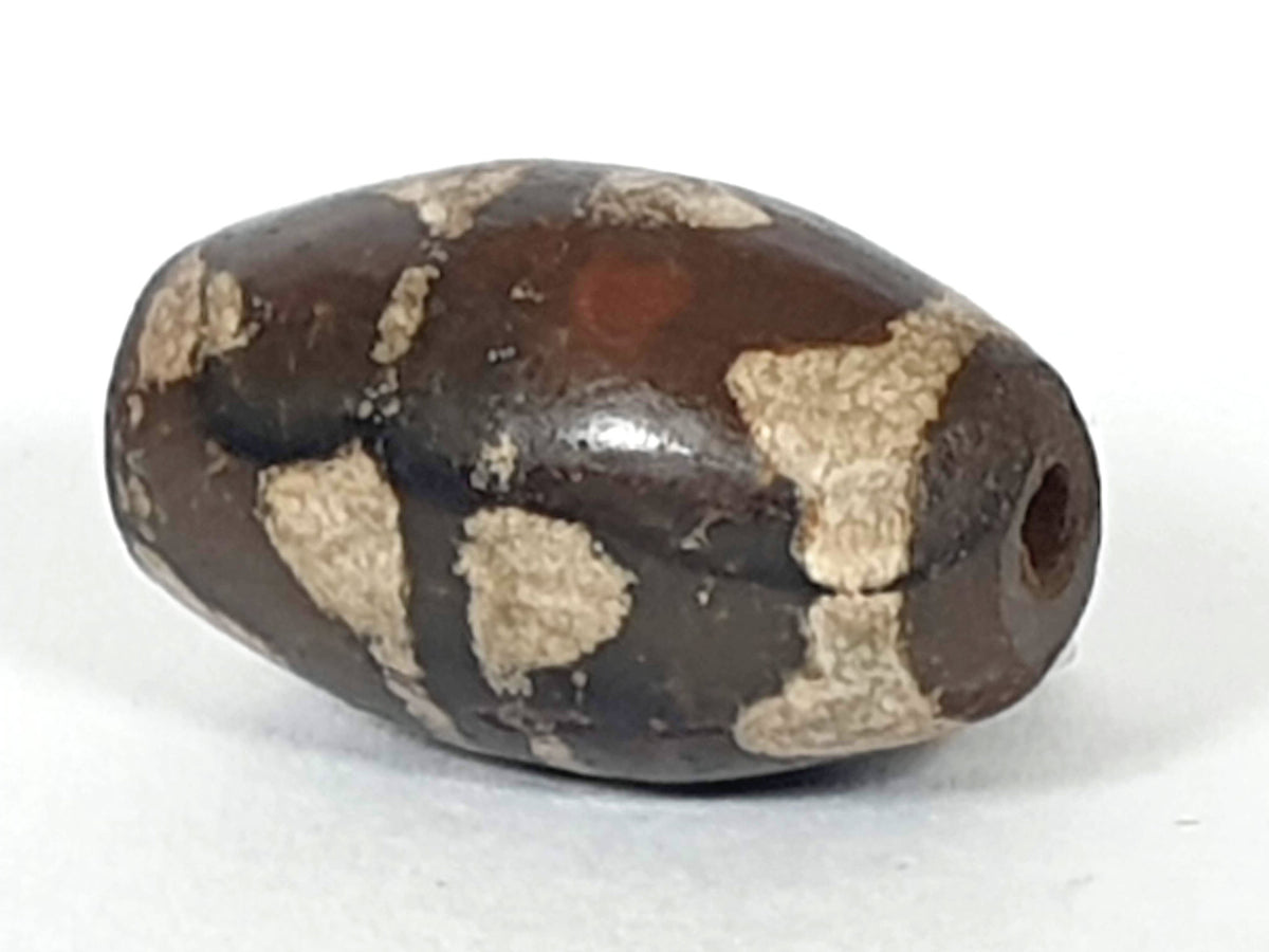 Antique double wave dzi — opposite angled end, drill hole at dark left tip, weathered cream wave zones on body, At-0426-DW2