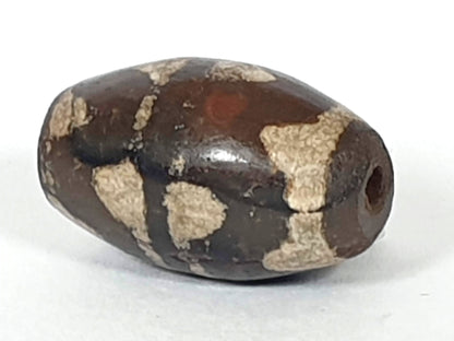 Antique double wave dzi — opposite angled end, drill hole at dark left tip, weathered cream wave zones on body, At-0426-DW2