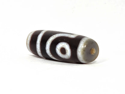 V-062126-2E dzi bead, angled view showing pale grey-white end cap and drill hole, unretouched