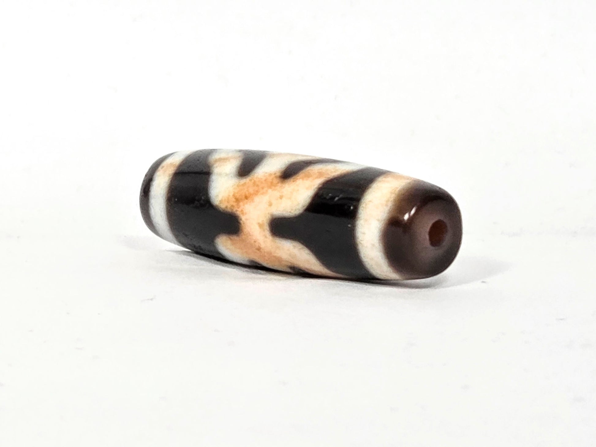 V-021326-BenBS vintage Benefactor dzi bead, angled end shot showing dark brown drill end cap and cream stripe, unretouched.