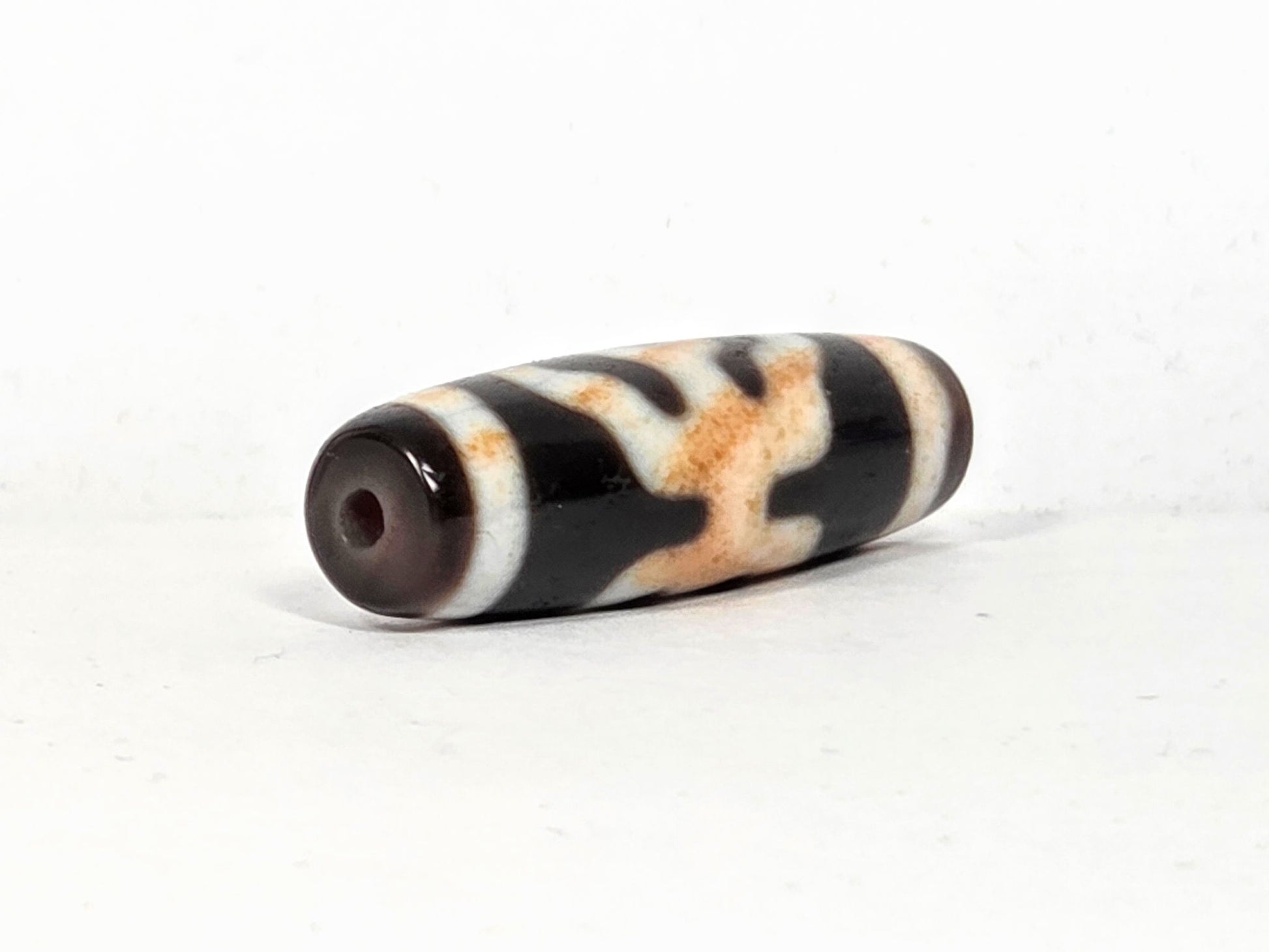 V-021326-BenBS vintage Benefactor dzi bead, second angled end shot, drill hole visible, dark brown end cap, unretouched.