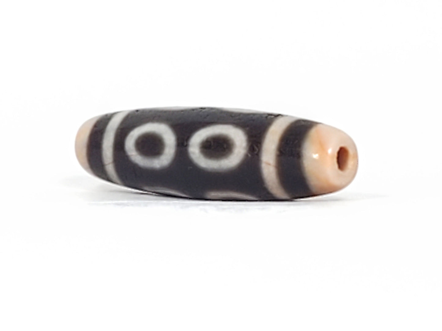 V-092924-8EBS Eight Eye dzi bead, angled end view, warm peachy-apricot end cap and drill hole visible, unretouched