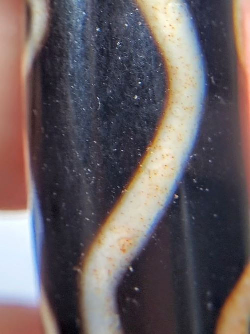 V-102723-6EBS Six Eye dzi bead, macro of wave connecting line showing scattered cinnabar inclusions, unretouched
