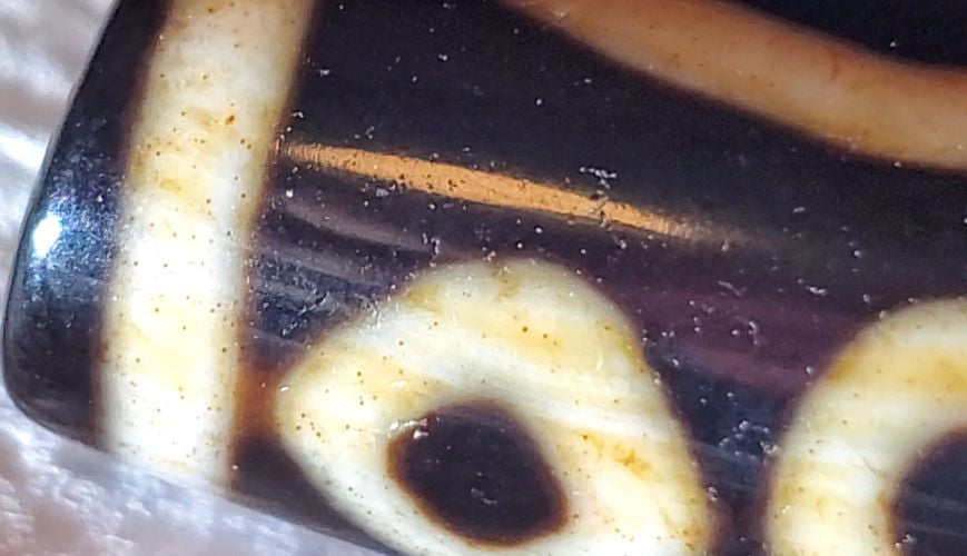 V-102723-6EBS Six Eye dzi bead, macro close-up showing cinnabar micro-dots in cream zones, unretouched
