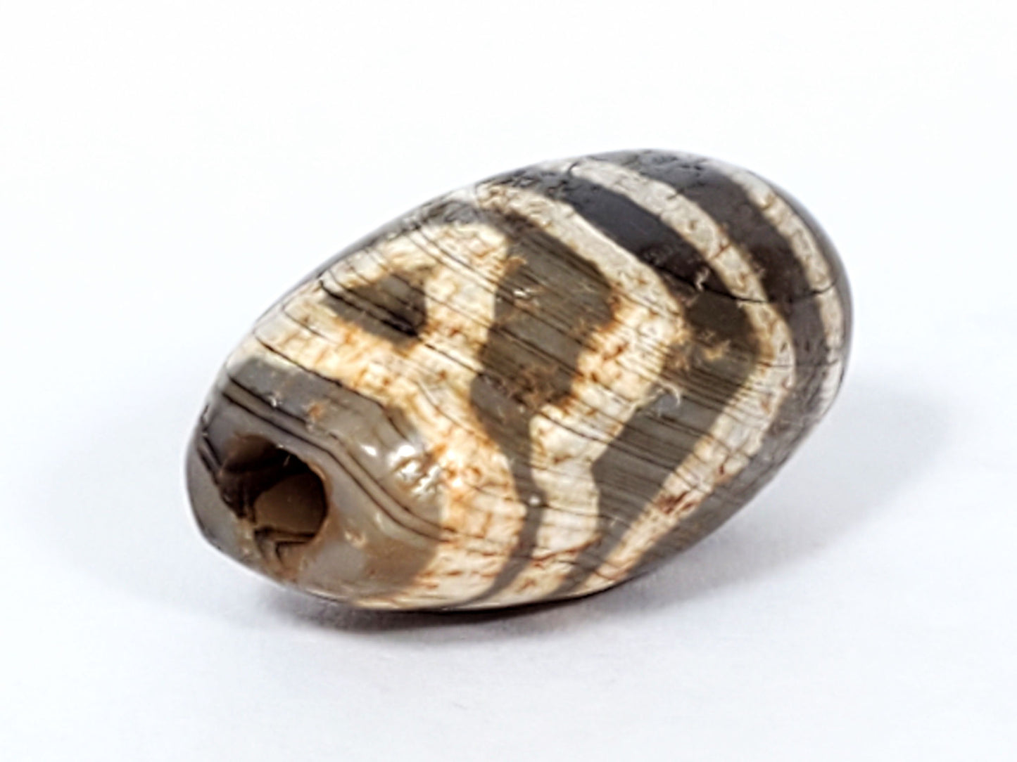 Angled end of ancient Two Eye Dzi bead — drill hole and cream stripe pattern, oval barrel profile