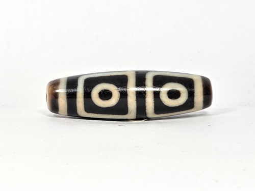 Antique Tibetan dzi bead, four-eye motif, black and white agate, oval barrel shape, visible drill hole, aged patina