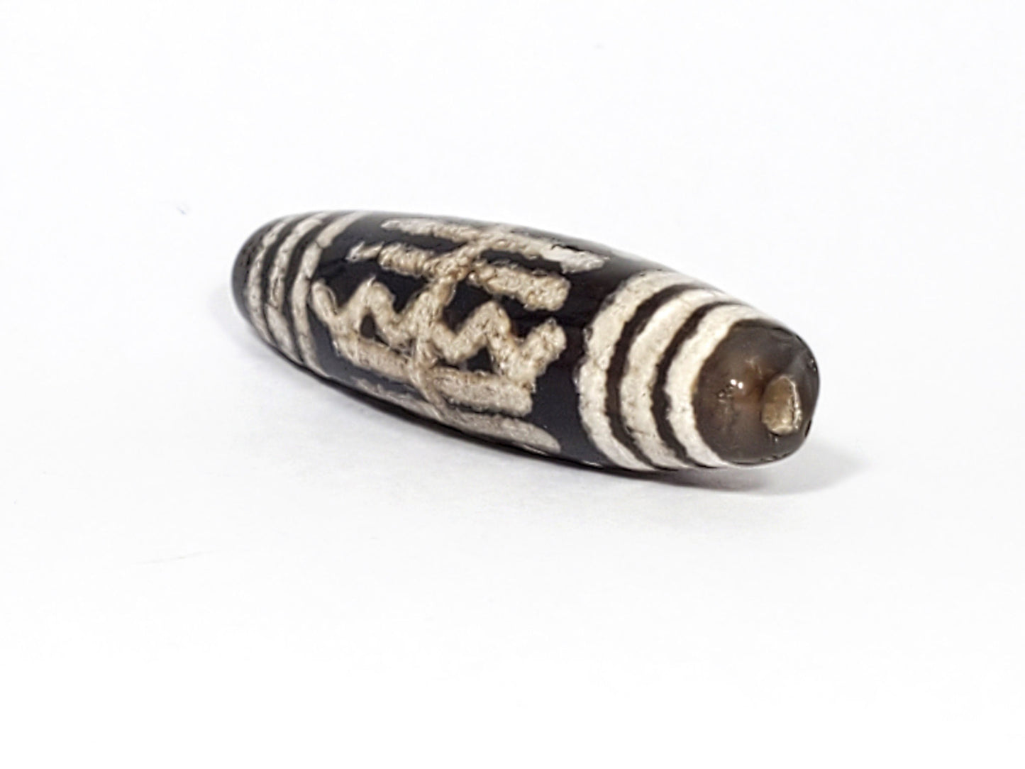 Angled end of antique Waves & Bars Dzi — drill hole, three cream bar stripes, warm brown agate tip