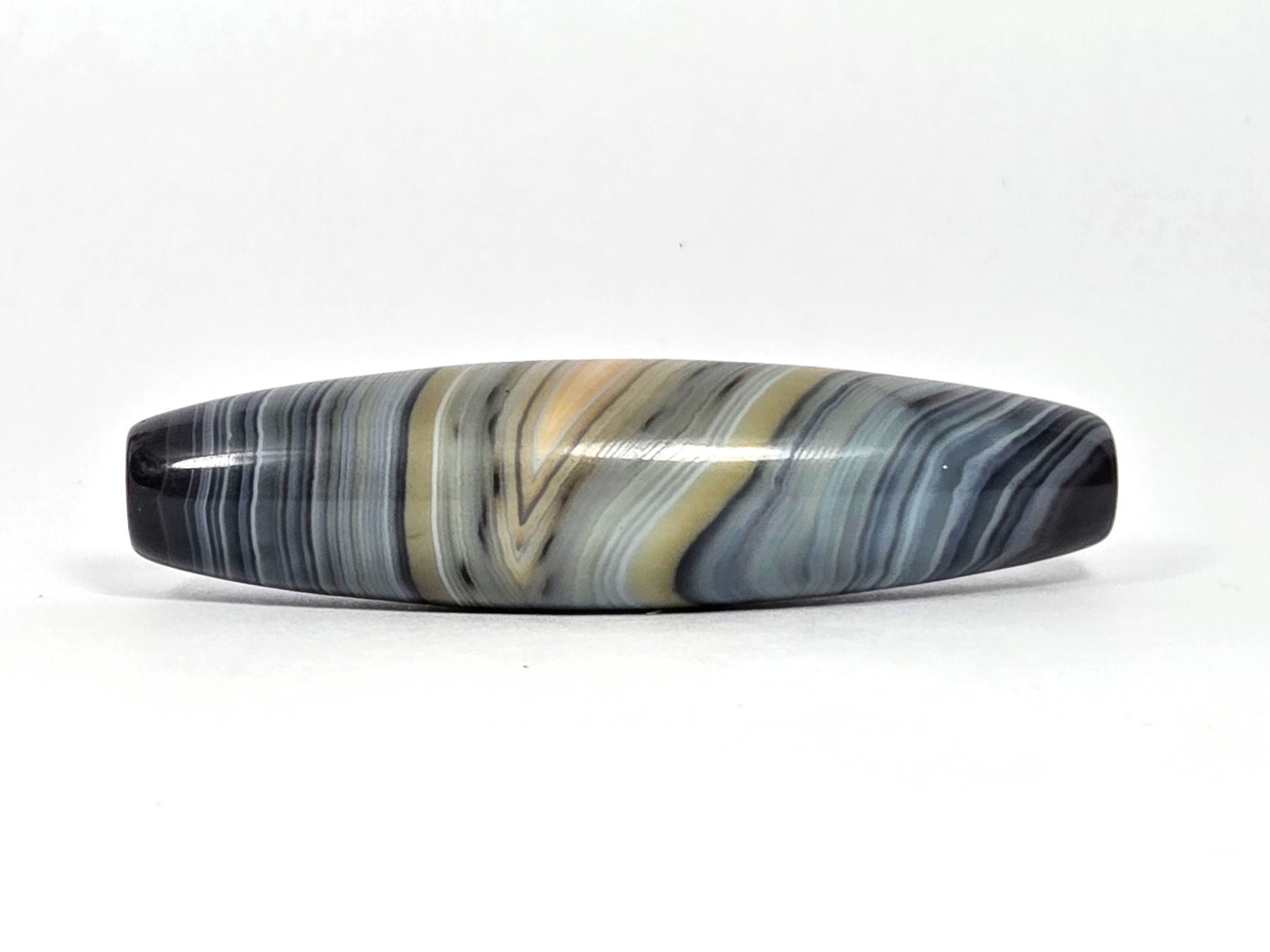 At-N-080426-1E2 antique natural one eye dzi bead 59.3×15.2mm, Face B showing warm gold zone in parallel blue-grey banding, eye partially dissolved, unretouched