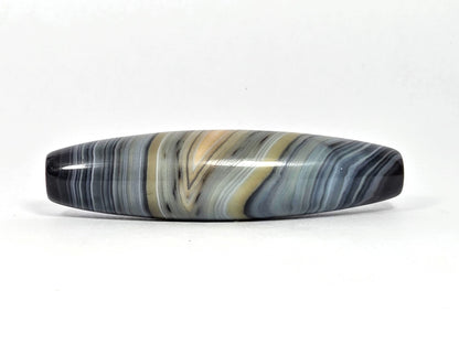 At-N-080426-1E2 antique natural one eye dzi bead 59.3×15.2mm, Face B showing warm gold zone in parallel blue-grey banding, eye partially dissolved, unretouched