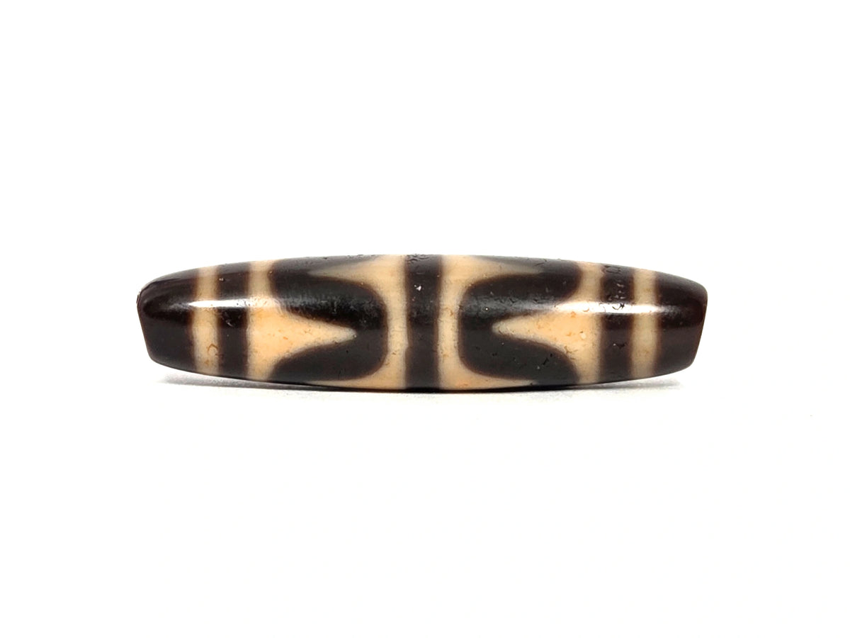 Antique Tibetan double wave dzi bead (AT-092926-DW4), first lateral profile showing dark brown and black opposing wave forms on honey-tan agate ground, 49.7 mm, 200–400 years old