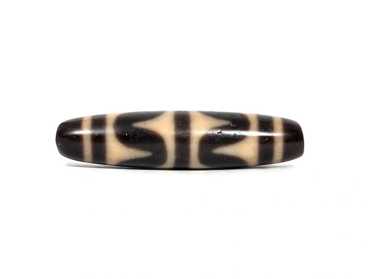 Third lateral profile of antique double wave dzi bead (AT-092926-DW4) showing full motif composition, dark brown and black wave forms on honey-tan ground, 49.7 mm × 11.9 mm