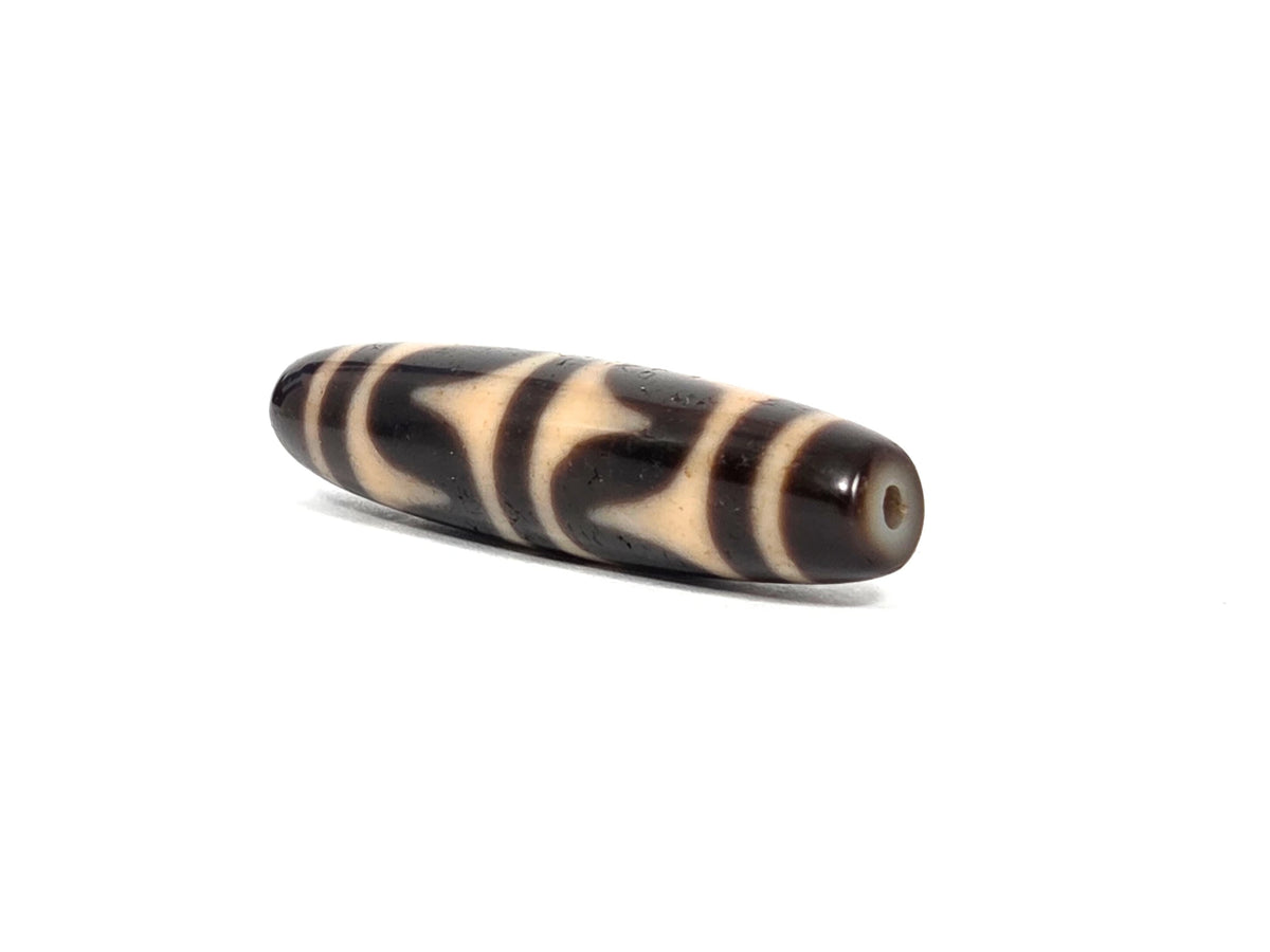Opposite end view of antique Tibetan double wave dzi bead (AT-092926-DW4) showing second drill hole and dark brown-black tip with honey-tan wave pattern continuing to the end