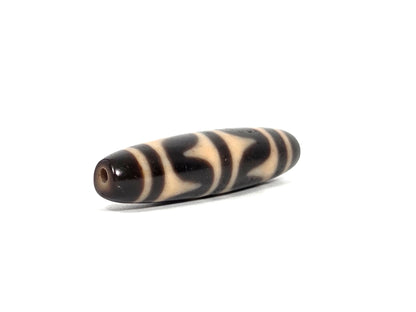 Angled end view of antique Tibetan double wave dzi bead showing small clean drill hole in deep dark brown agate tip, elongated barrel form, 200–400 years old