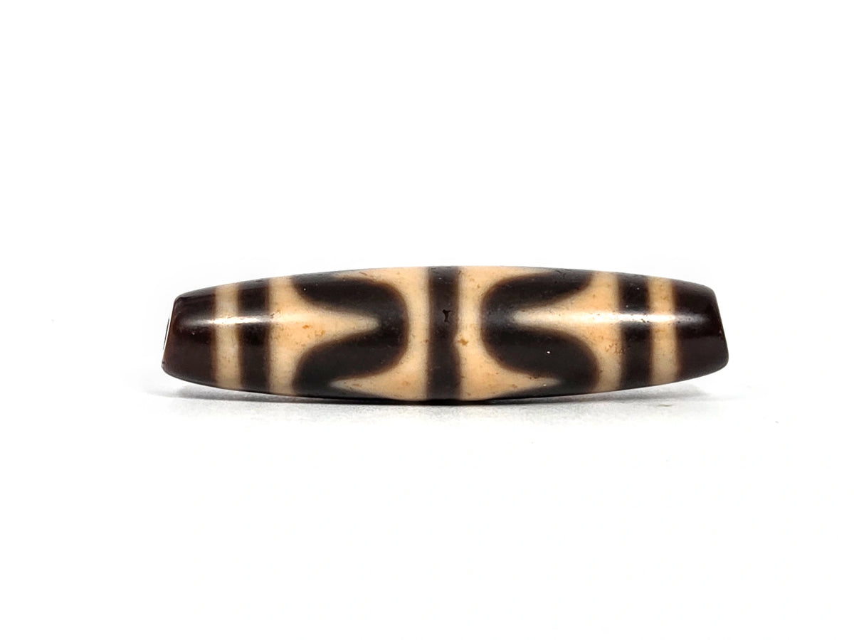 Antique Tibetan double wave dzi bead (AT-092826-DW3), first lateral profile showing dark brown opposing wave forms in three panels on warm honey-tan agate ground, 49.7 mm, 200–400 years old