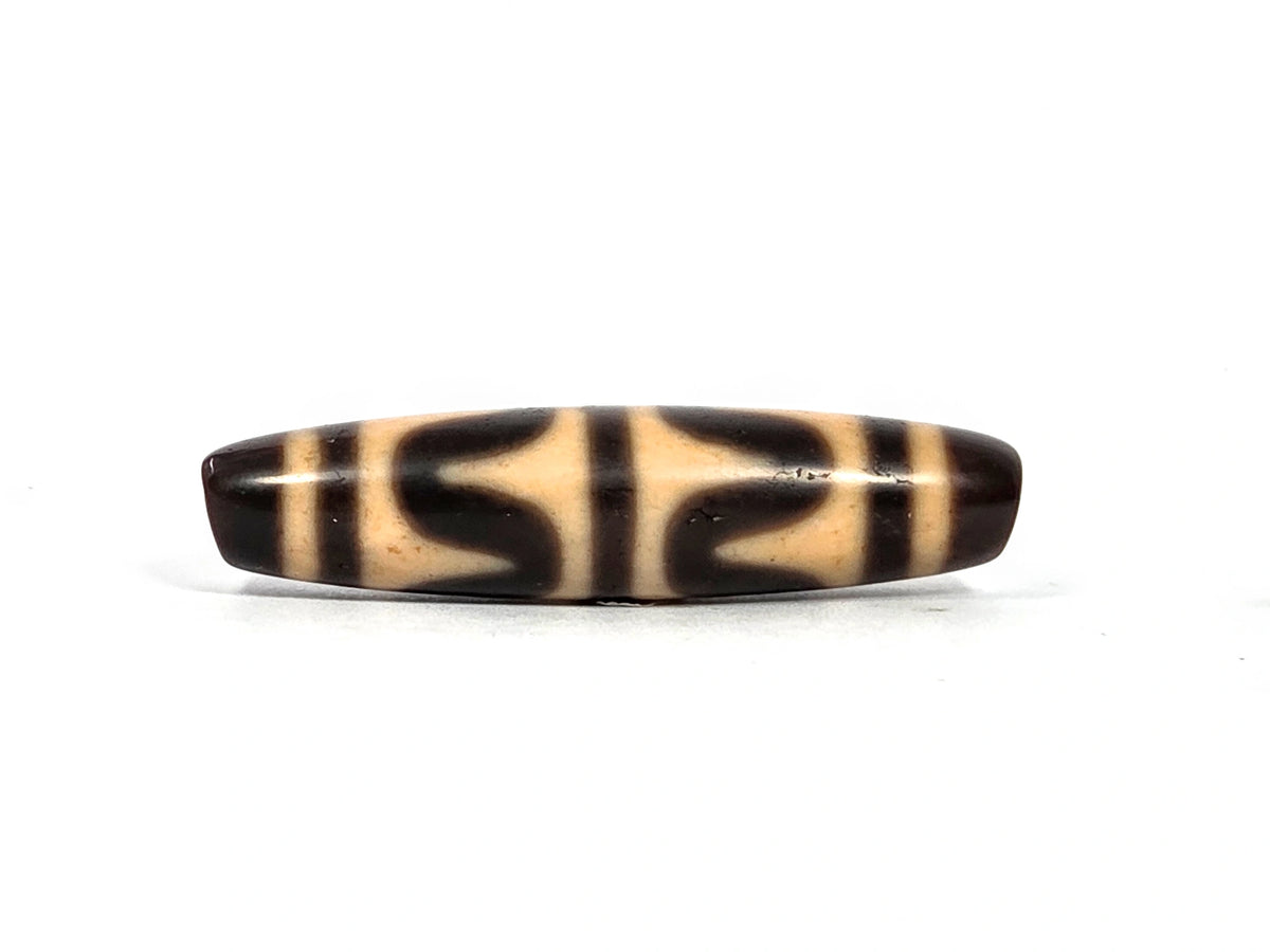 Third lateral profile of antique double wave dzi bead (AT-092826-DW3) showing full motif composition, dark brown wave forms on warm cream-tan ground, 49.7 mm × 11.9 mm