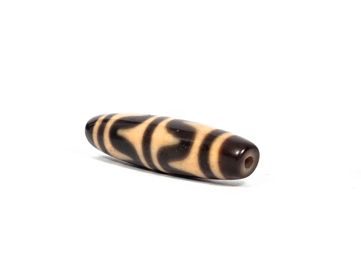 Opposite end view of antique Tibetan double wave dzi bead (AT-092826-DW3) showing second drill hole and dark brown agate tip with warm honey-tan wave pattern continuing to the end