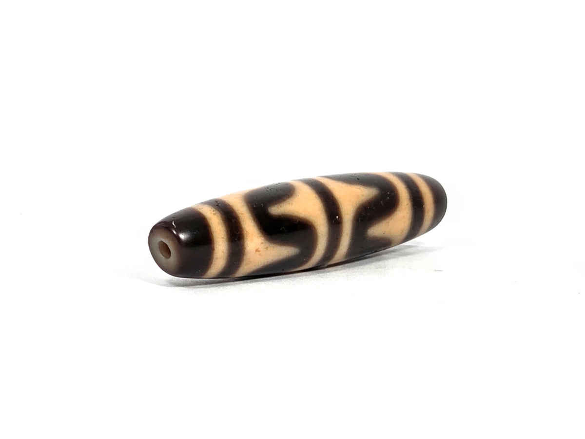 Angled end view of antique Tibetan double wave dzi bead showing small clean drill hole set in deep dark brown agate tip, 200–400 years old, elongated barrel form